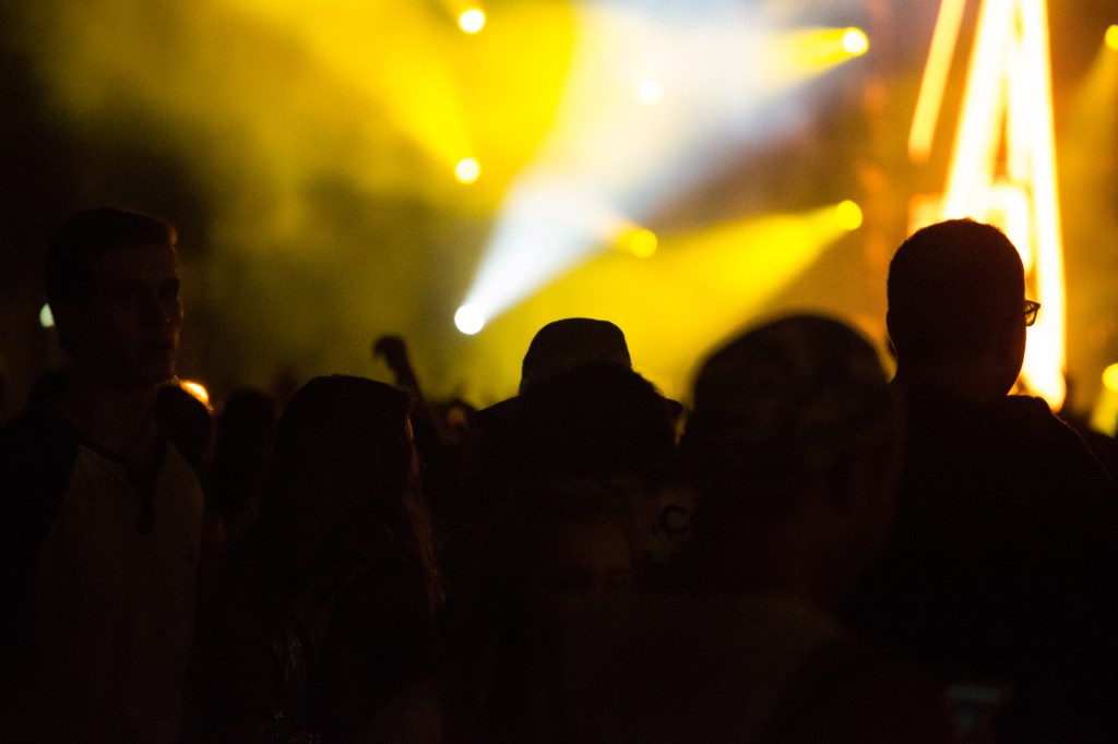 A crowd of people at Lollapalooza with yellow and blue stage lights illuminating the scene.