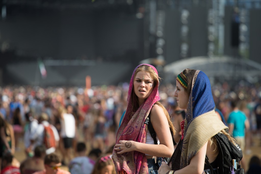 Two young women wearing colorful scarves and face paint, standing in a large crowd at Lollapalooza.