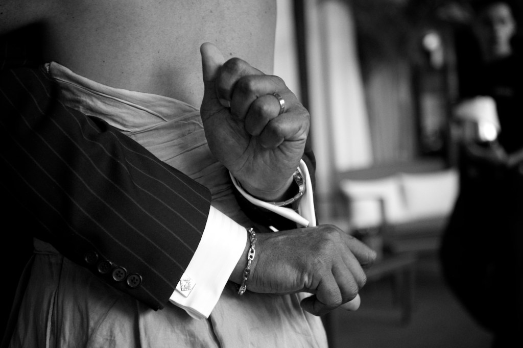 Close-up of two elegant hands, one in a striped suit and the other adorned with a bracelet, intertwined against a blurred background.